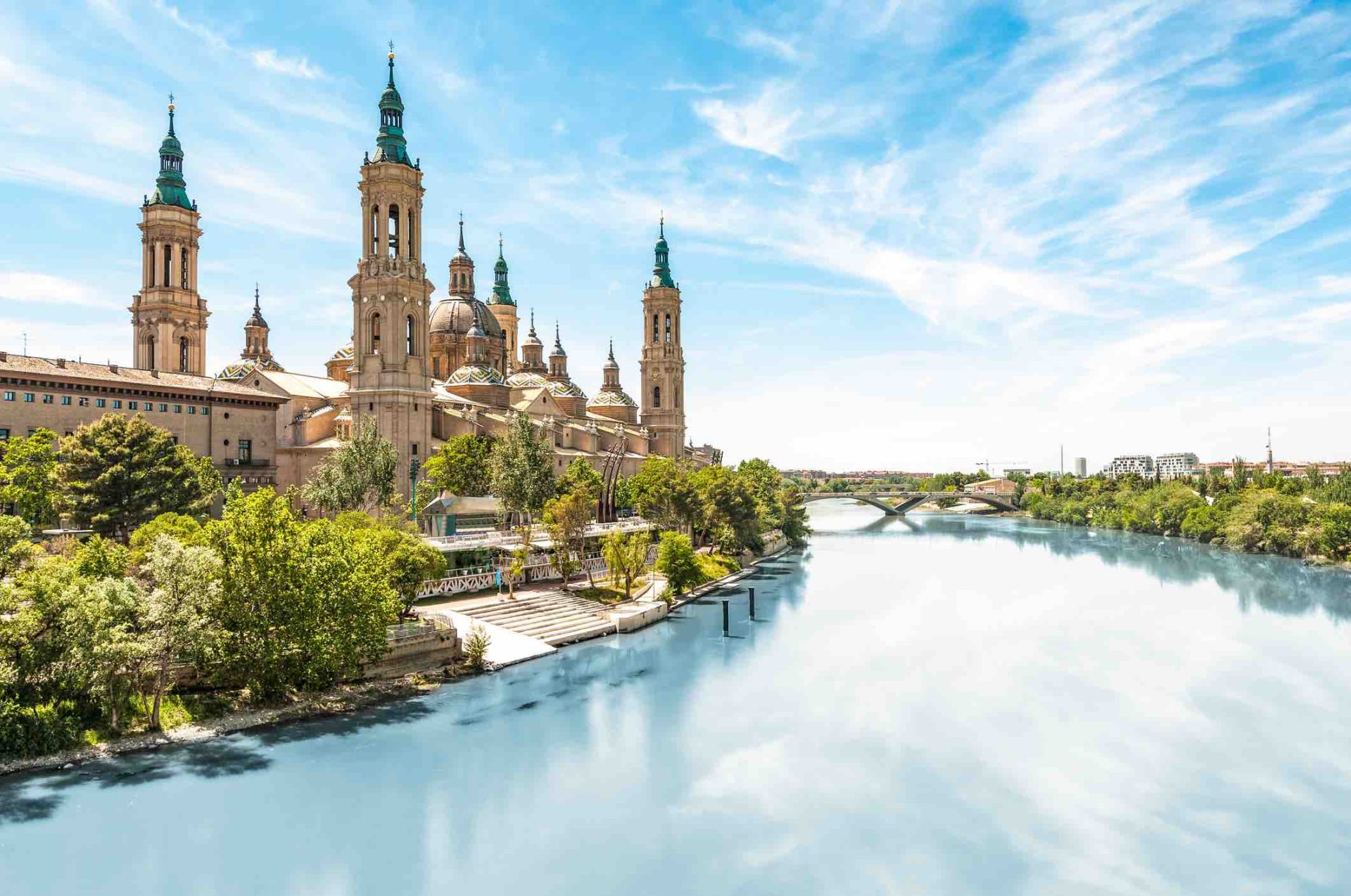 Scenery landscape with Basilica of Our Lady of Pillar. Blue sky reflects in clear water. Green trees along river. Famous church with beautiful architecture. Famous tourist place in Spain, Europe. Zaragoza