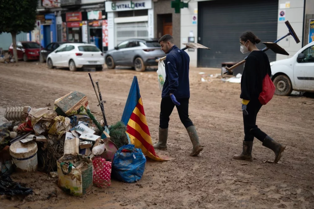 Dos personas con palas observan una bandera de la Comunidad Valenciana mientras pasan por una calle de Benetússer, a 4 de noviembre de 2024, en Benetússer, Valencia, Comunidad Valenciana (España)