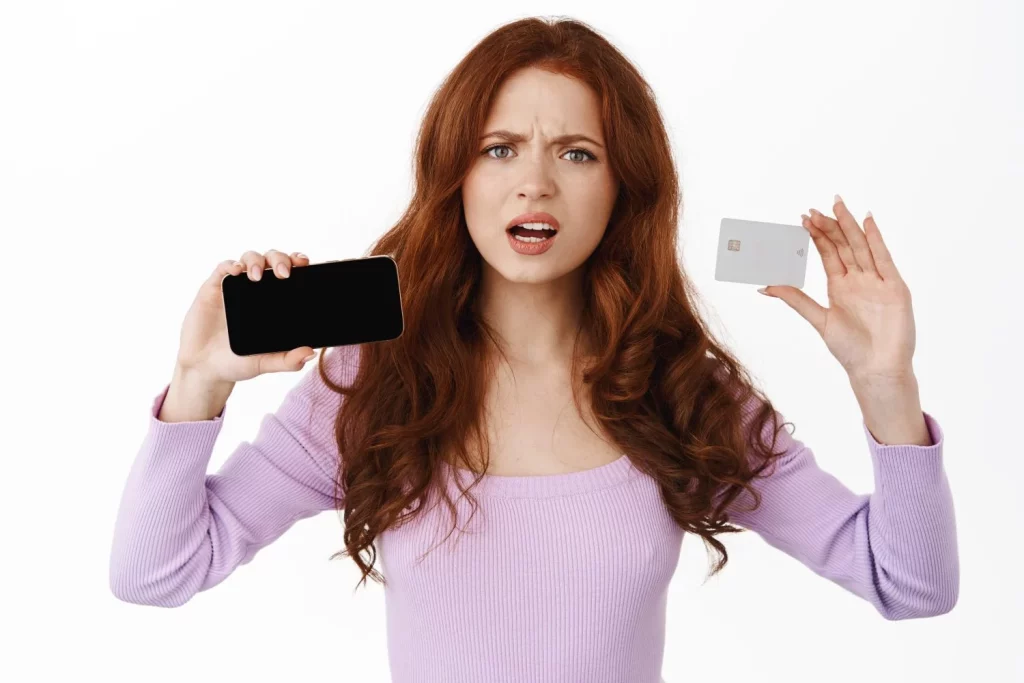 El truco de los ciberdelincuentes para descubrir tu contraseña aunque sea segura 4 Moncloa woman shows horizontal smartphone screen credit card frowning looking disappointed complaining about something phone standing white Moncloa