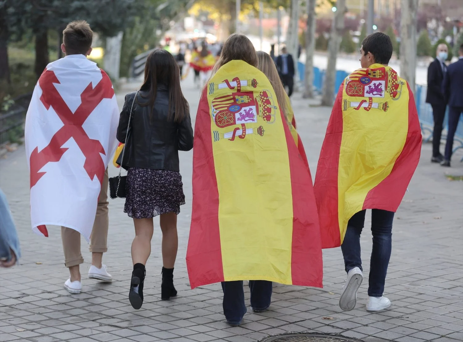 Un joven con la bandera de la Cruz de Borgoña (i) y otros tapados con la bandera de España se dirigen acto solemne de homenaje a la bandera nacional y desfile militar en el Día de la Hispanidad