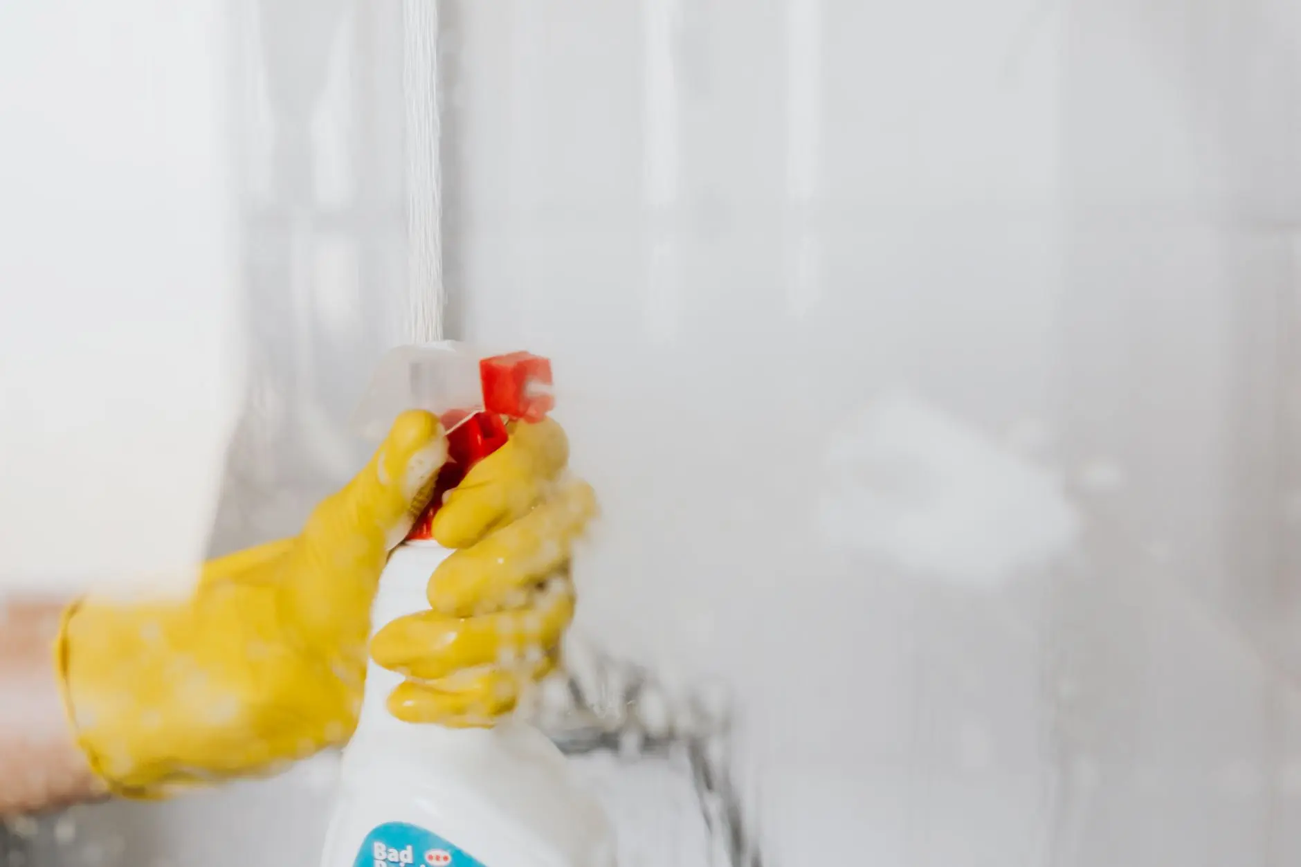 Persona usando guantes amarillos limpiando una superficie de vidrio con una botella de spray.
