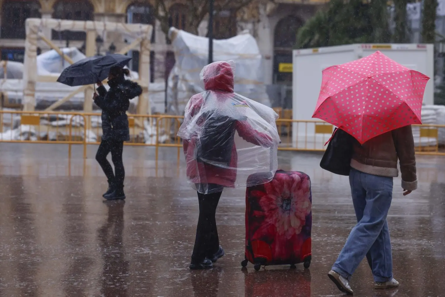 Personas caminan ante ninots tapados con plásticos por la lluvia durante el montaje de las Fallas 2026. Fuente: Agencias Personas caminan ante ninots tapados con plásticos por la lluvia durante el montaje de las Fallas 2026. Fuente: Agencias