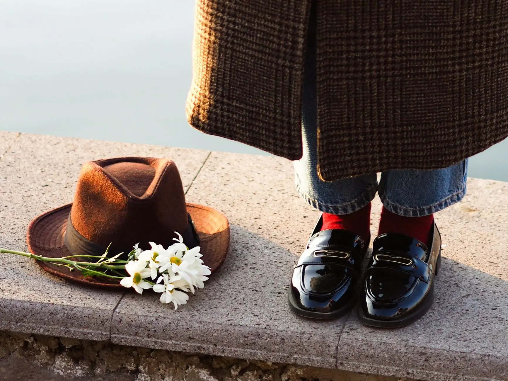 Primer plano de un elegante atuendo con zapatos, sombrero y margaritas junto a un río.