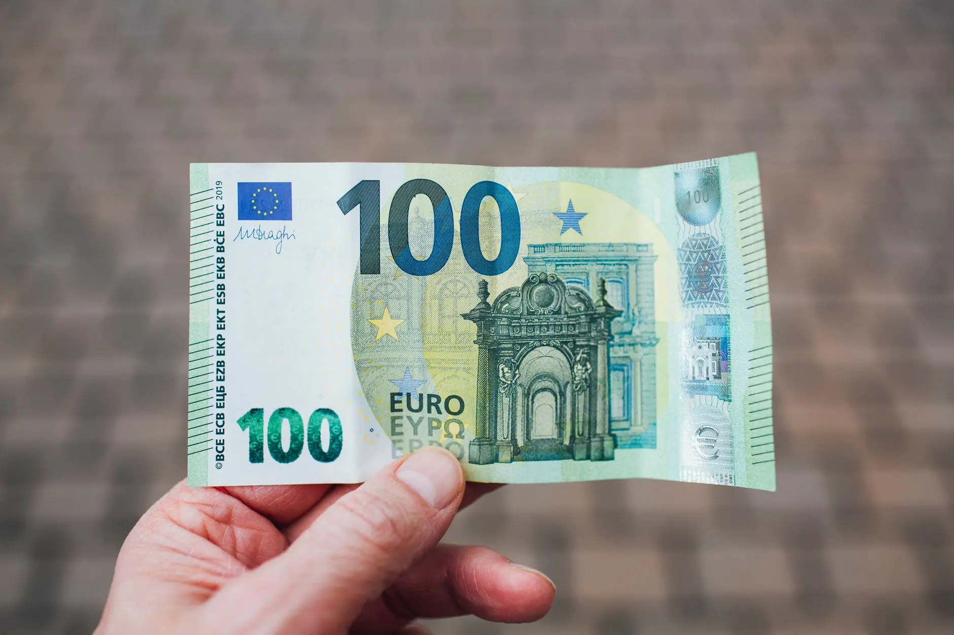 Foto en primer plano mostrando a una persona sosteniendo un billete de 100 euros contra un fondo difuminado.