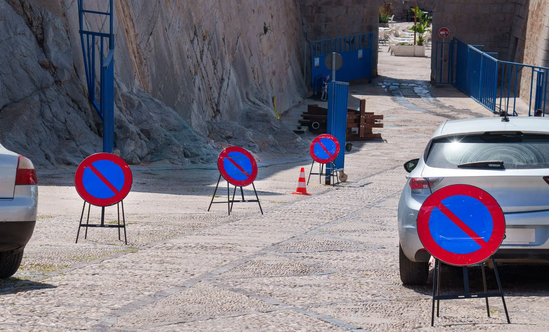 Una hilera de señales de prohibido aparcar en una calle empedrada con coches aparcados, lo que subraya las restricciones de circulación.